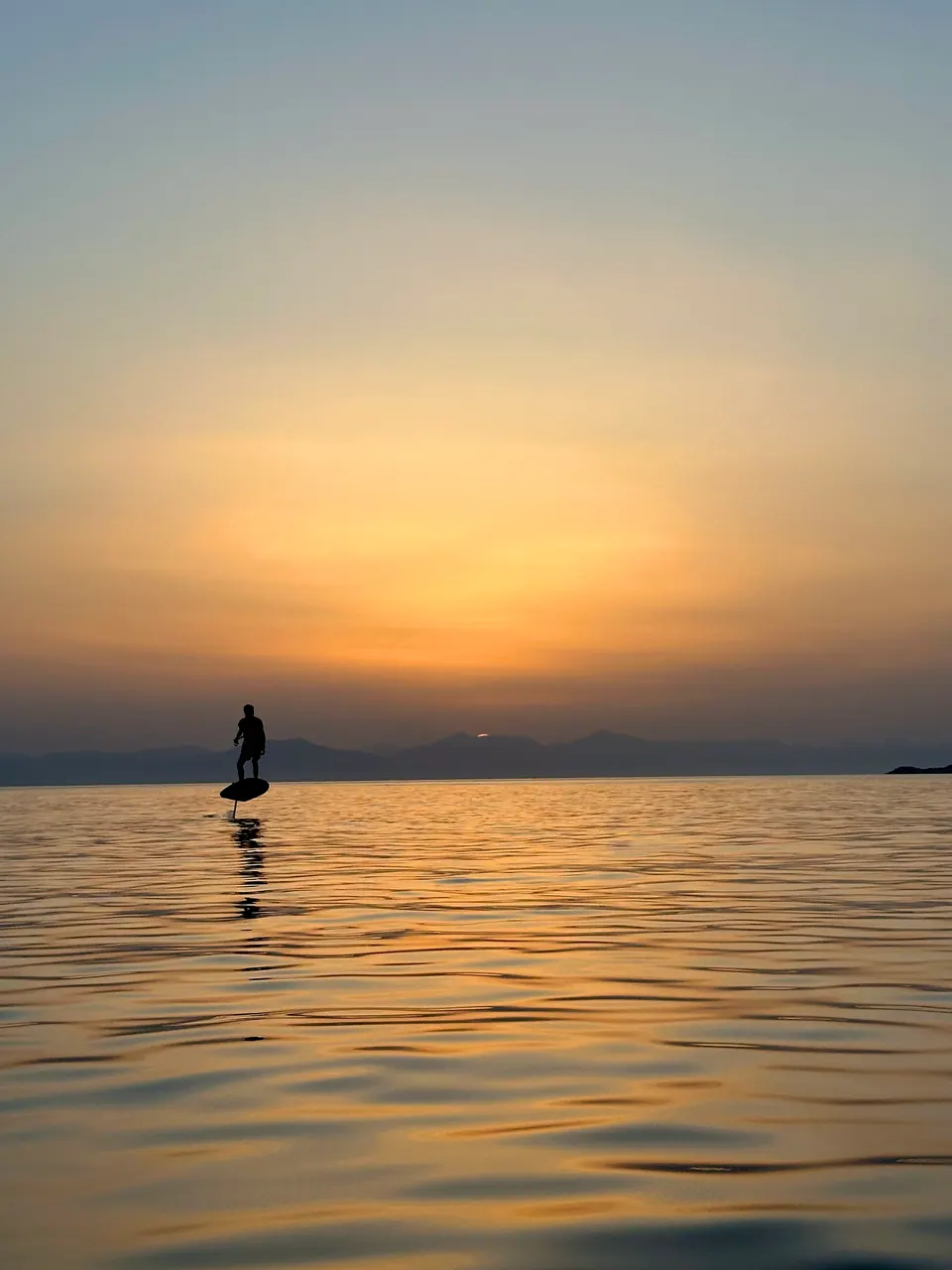 Silhouette of a rider on an electric hydrofoil board over calm water at sunset